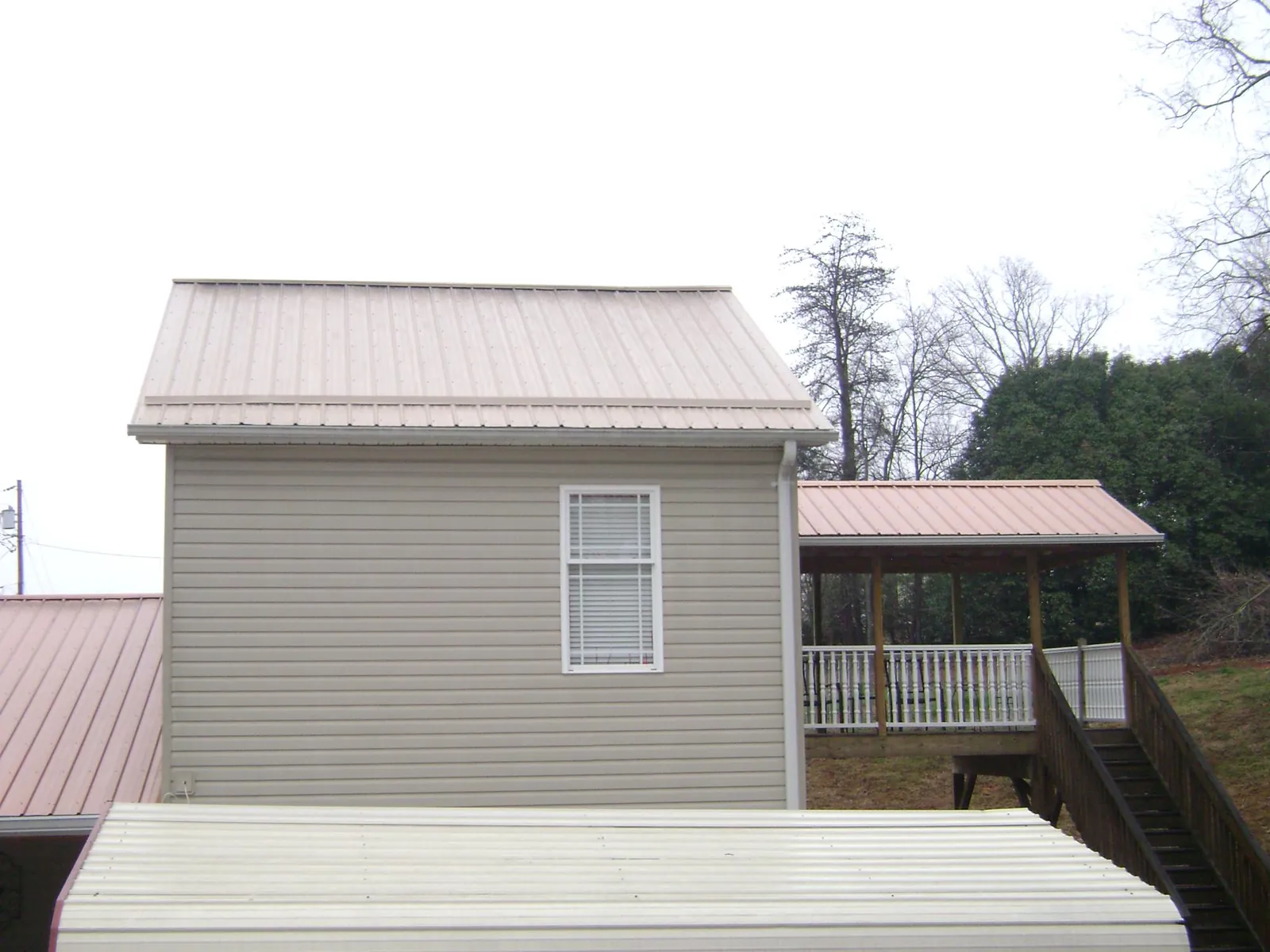 Tan metal roofs on a two story addition and attached porch, from a Roof Replacement job in Cleveland